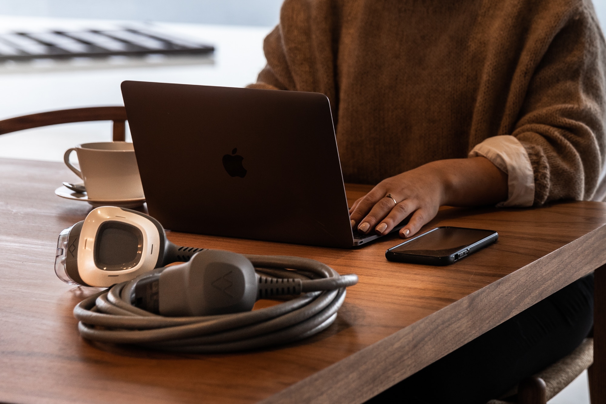 Woman sits with a laptop and a charging cable lays on a table